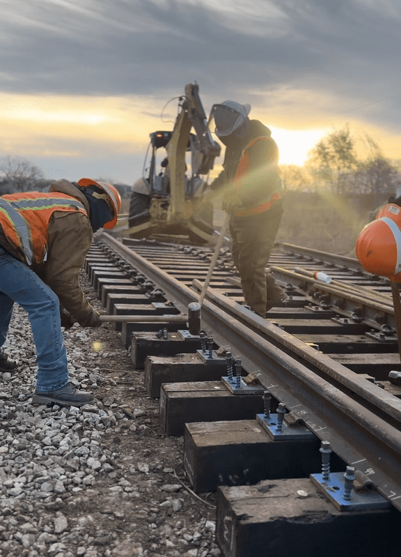 Workers installing railway tracks during sunrise.