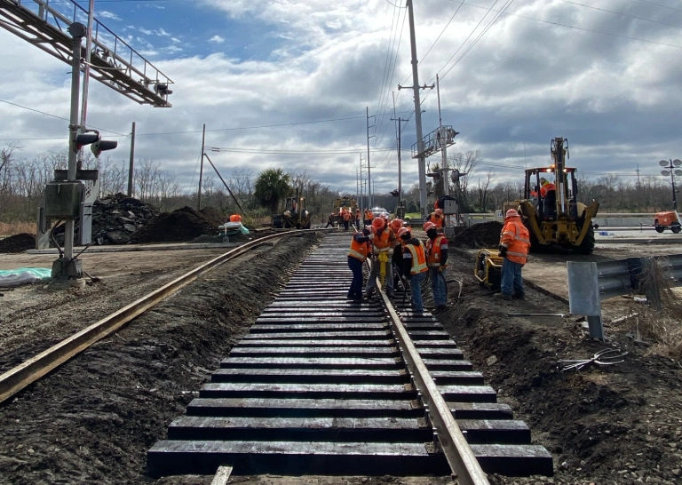 Workers are repairing railroad tracks under a cloudy sky.