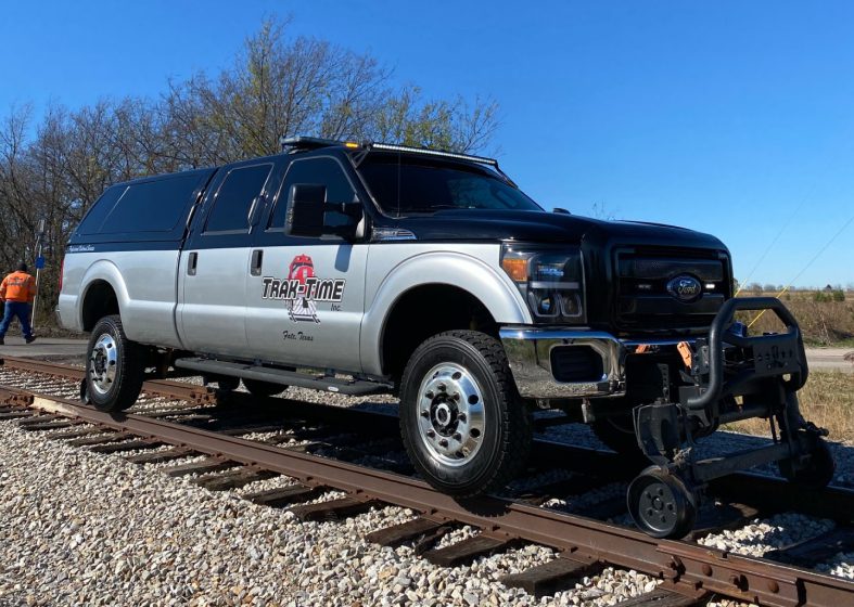 A silver pickup truck on railroad tracks under a clear blue sky.