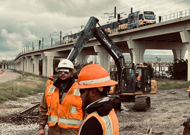 Construction workers at a railway bridge site with heavy machinery.