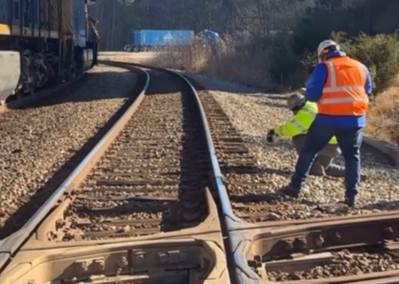 A railway worker inspecting train tracks with tools in hand.
