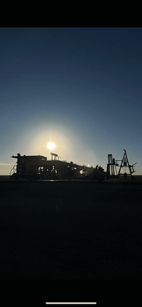 Silhouette of industrial cranes and structures against a setting sun.